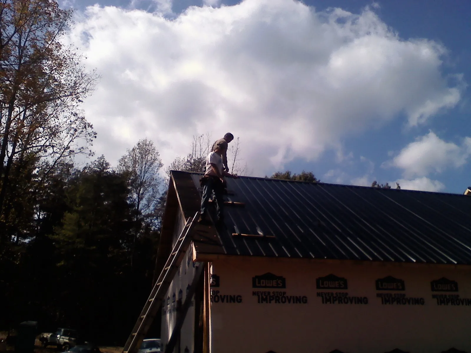 Roofer fastening dark metal panels high against a cloudy sky, from a Roof Inspection job in Mendon